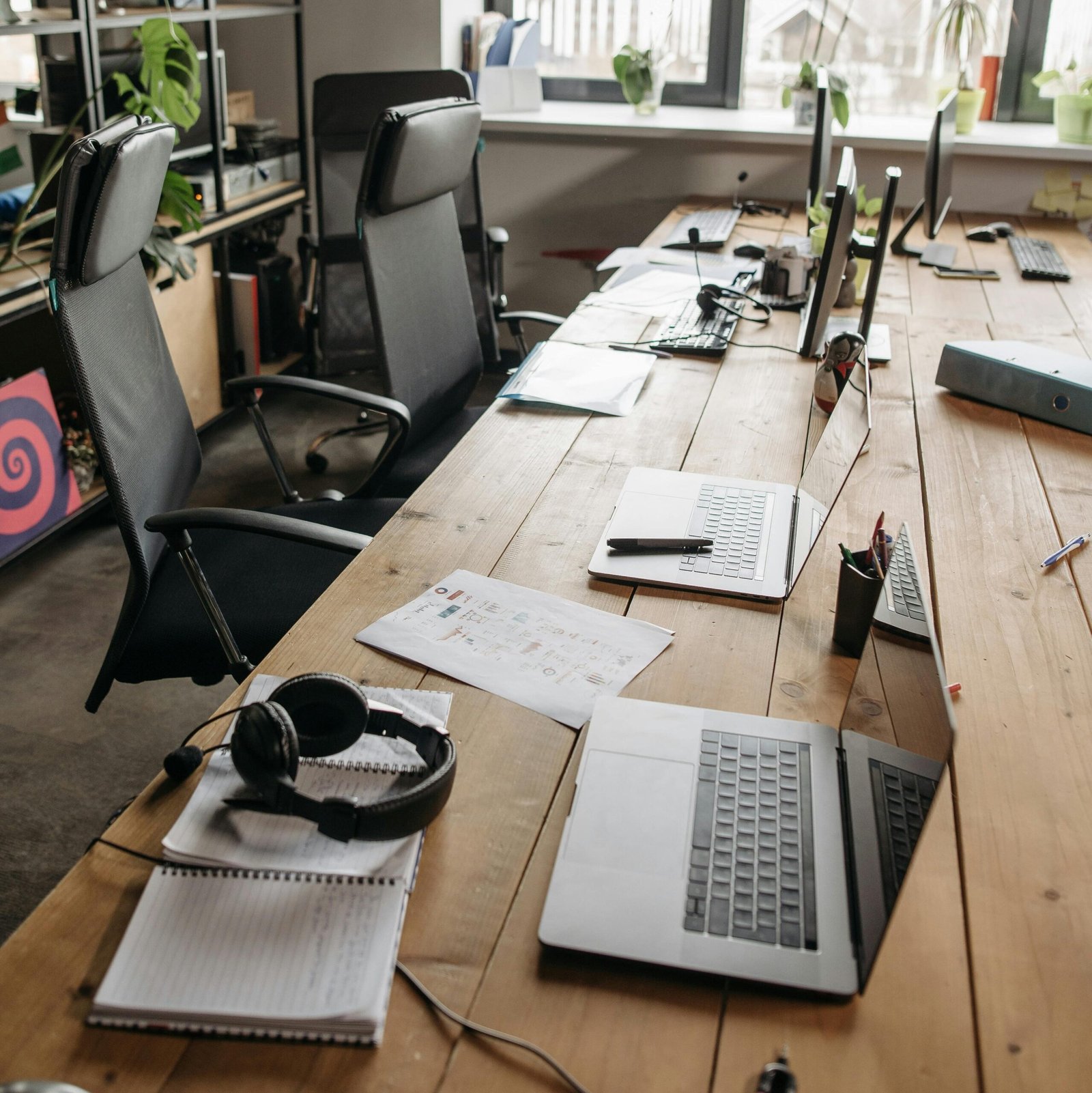 A contemporary office setting with laptops and chairs around a wooden table, ideal for teamwork.